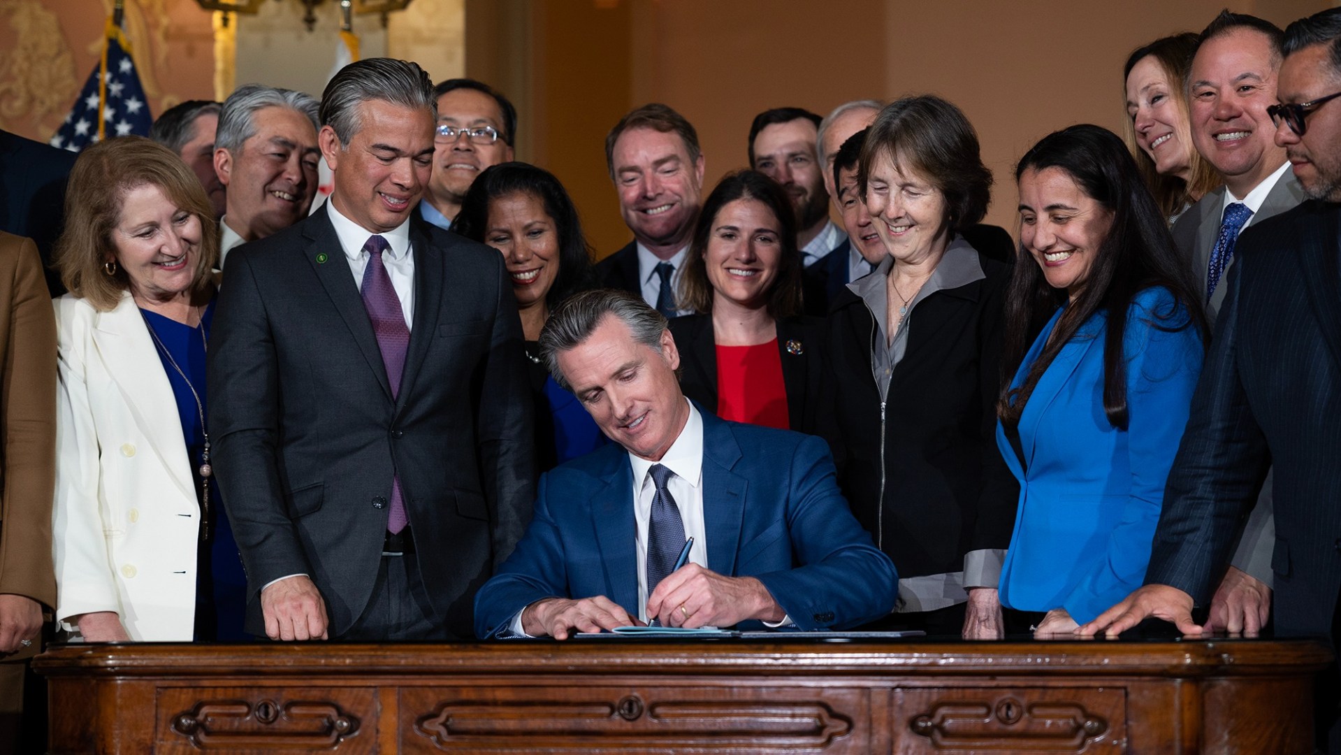 Gov. Gavin Newsom is surrounded by lawmakers as he signs into law his oil profit penalty plan in Sacramento on March 28, 2023. Photo by Miguel Gutierrez Jr., CalMatters